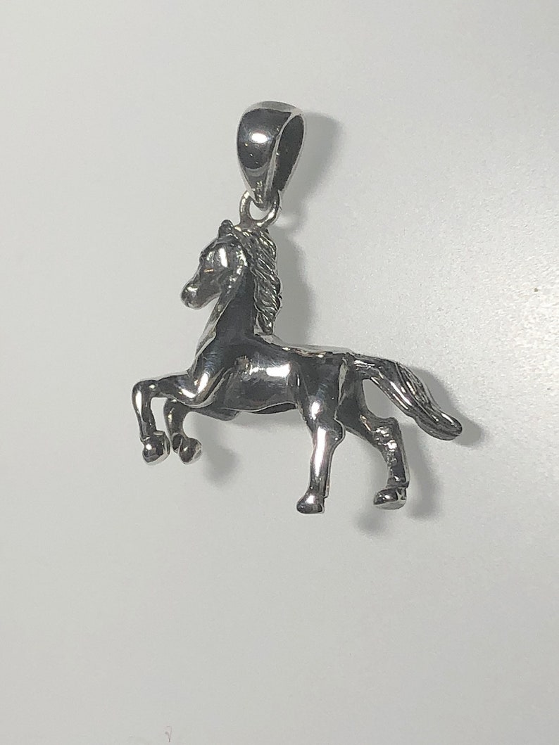 May include: A silver horse pendant charm. The horse is standing on all four legs with its head held high. The pendant has a loop at the top for attaching to a chain or bracelet.