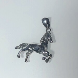 May include: A silver horse pendant charm. The horse is in a running pose with its head turned to the side. The pendant has a loop at the top for attaching to a chain.