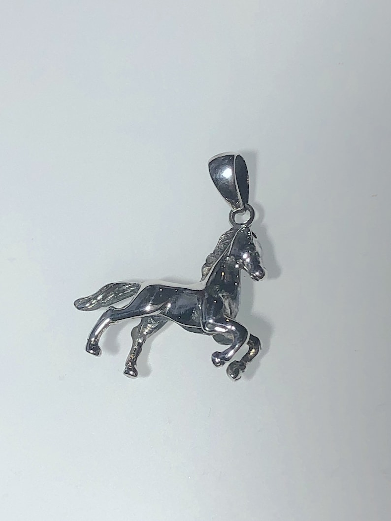 May include: A silver horse pendant charm. The horse is in a running pose with its head turned to the side. The pendant has a loop at the top for attaching to a chain.