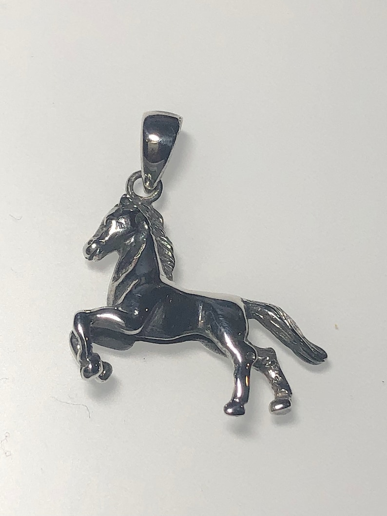 May include: Silver horse pendant charm. The horse is standing on its hind legs with its head turned to the side. The pendant has a loop at the top for attaching to a chain or bracelet.