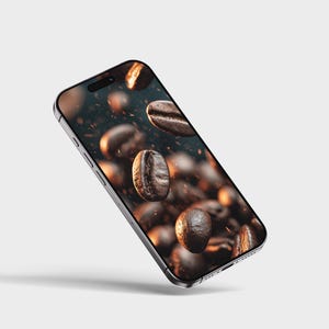 May include: A smartphone displays a close-up image of roasted coffee beans in mid-air. The beans are various shades of brown, with some appearing glossy. The phone has a silver frame and a black screen.