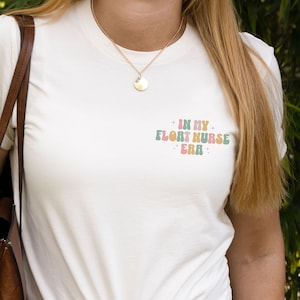 May include: A white t-shirt with the text "In My Float Nurse Era" in a retro font with colorful letters.