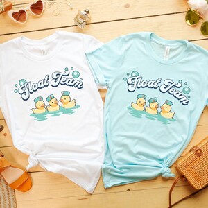 May include: Two white t-shirts with a light blue t-shirt on top. The t-shirts have a graphic of three yellow rubber ducks wearing blue and white sailor hats and the text "Float Team" in a retro font.