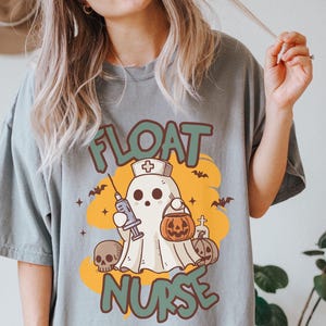May include: A gray t-shirt with a cartoon ghost wearing a nurse's hat and holding a syringe and a bucket of candy. The text "FLOAT NURSE" is printed on the shirt.