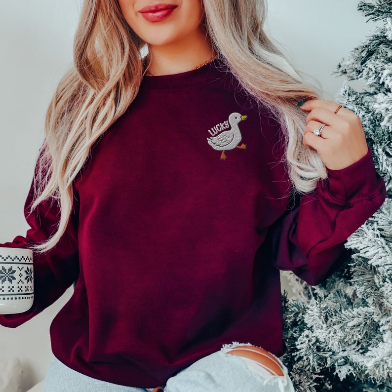 May include: A maroon sweatshirt with a white embroidered goose and the word "LUCKY" on the front.