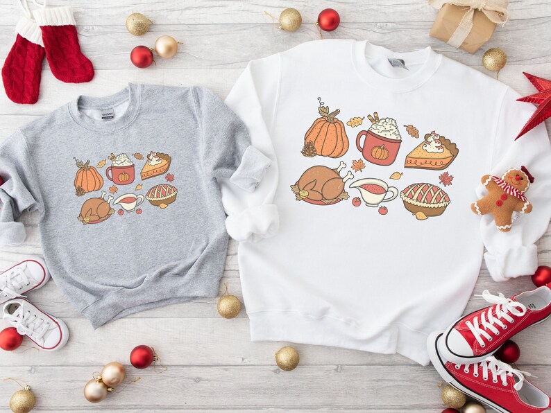 May include: Two gray and white sweatshirts with Thanksgiving-themed graphics. The gray sweatshirt features a turkey, pumpkin, pie, and a cup of coffee with whipped cream. The white sweatshirt features a turkey, pumpkin, pie, and a cup of coffee with whipped cream.