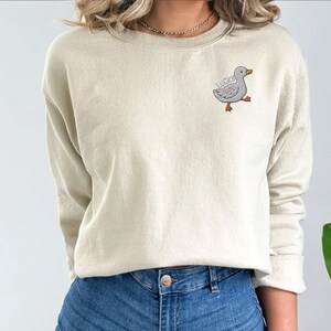 May include: A cream colored sweatshirt with a gray embroidered duck with the word "lucky" on it.