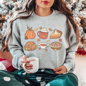May include: A gray sweatshirt with a Thanksgiving-themed design featuring a pumpkin, a turkey, a pie, a cup of coffee, and a bowl of gravy. The design is in a cartoon style with bright colors.