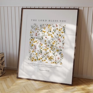 Pode incluir: Uma impressão emoldurada com o texto "THE LORD BLESS YOU" no topo. A impressão apresenta um padrão floral com flores amarelas, rosa e brancas. A parte inferior da impressão inclui texto de Números 6:24-26.