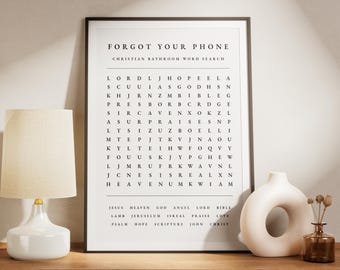 May include: A framed Christian bathroom word search print with the text "FORGOT YOUR PHONE". The print is black and white and is displayed on a wooden surface next to a white lamp and decorative vases.