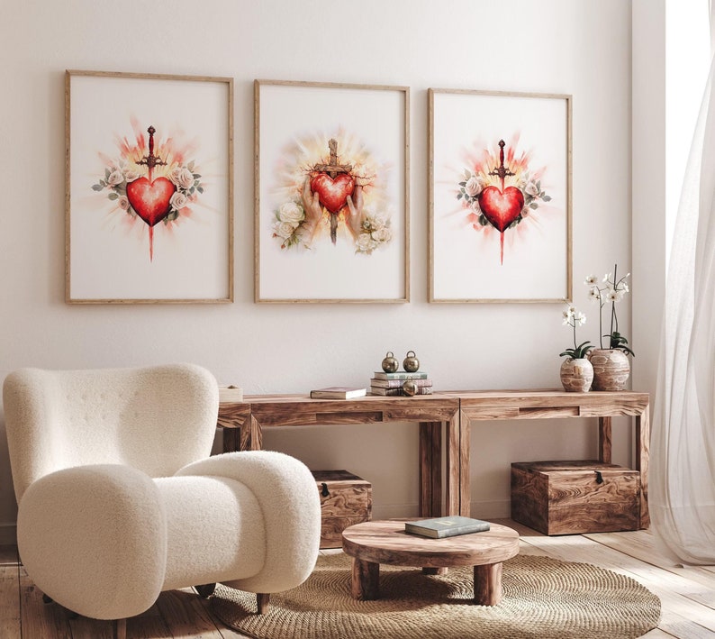 Pode incluir: Tr&ecirc;s pinturas em aquarela emolduradas que retratam um cora&ccedil;&atilde;o vermelho atravessado por uma espada, rodeado de rosas brancas e uma luz radiante. O cora&ccedil;&atilde;o &eacute; um s&iacute;mbolo do Sagrado Cora&ccedil;&atilde;o de Jesus.