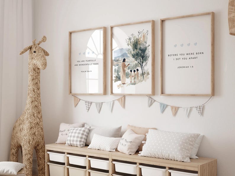 May include: Three framed prints with inspirational quotes and watercolor illustrations. The prints feature the text "You are fearfully and wonderfully made", "Before you were born I set you apart", and a watercolor illustration of Jesus with two children. The prints are hung on a white wall with a garland of blue and white flags.