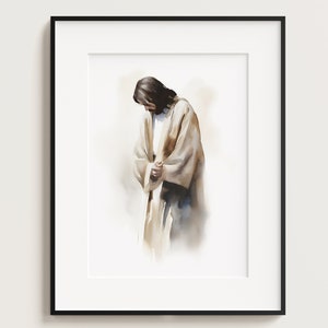 May include: Watercolor painting of a figure in a long, flowing robe, head bowed in a gesture of reverence. The artwork features soft, muted tones of beige, brown, and blue, set against a white background. The framed print is a religious art piece.
