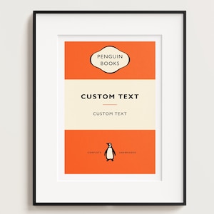 Puede incluir: Impresión enmarcada con un diseño de Penguin Books. La obra de arte tiene una combinación de colores naranja y crema con las palabras "Penguin Books" en la parte superior. Las palabras "Custom Text" aparecen en el centro y una ilustración de pingüino en la parte inferior.