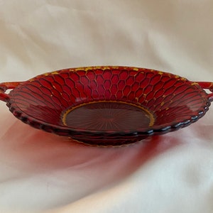 May include: A red glass serving dish with two handles. The dish has a honeycomb pattern and a gold rim.