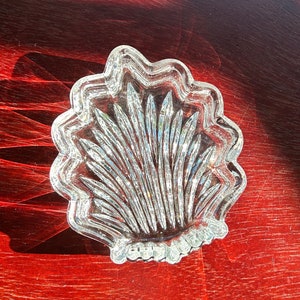May include: A clear glass dish with a scalloped edge and a fan-shaped design. The dish is made of crystal and has a delicate, elegant look.