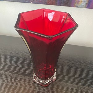 May include: A red glass vase with a hexagonal opening and a clear, faceted base.