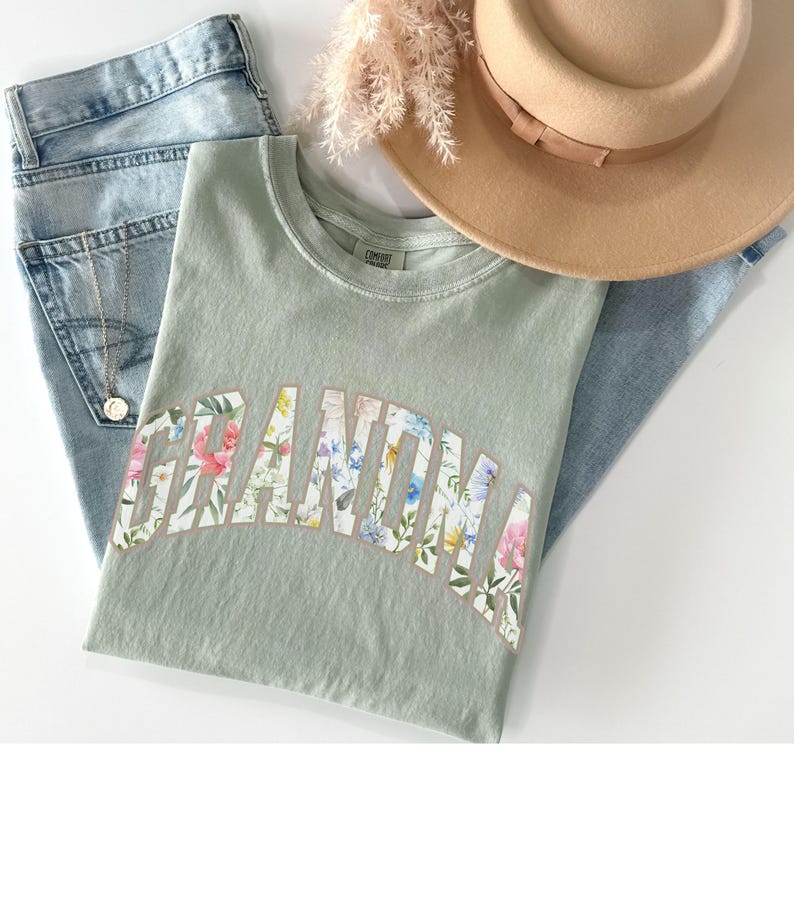May include: A light green t-shirt with a floral print design that spells out the word "Grandma".