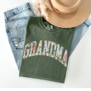 May include: A green t-shirt with a floral print design that spells out "Grandma".