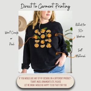 May include: A black sweatshirt with a design of orange slices and flowers. The text "Direct to Garment Printing" is at the top of the image. The text "Won't Crack or Peel" is on the left side of the image. The text "Rated for 50+ Washes" and "Soft Material" are on the right side of the image. The text "IF YOU WOULD LIKE ANY OF MY DESIGNS ON A DIFFERENT PRODUCT - TSHIRT, MUGS, ORNAMENTS ETC. PLEASE LET ME KNOW I WOULD BE HAPPY TO DO THAT FOR YOU" is at the bottom of the image.
