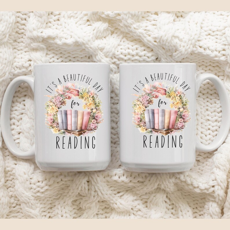 May include: Two white ceramic mugs with a floral wreath design and the text "It's a beautiful day for reading." The design includes a stack of books in pastel colors. The mugs have large handles.