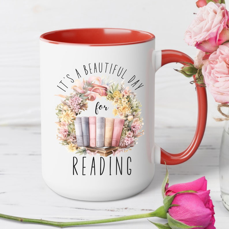 May include: White ceramic mug with a red interior and handle. The mug features the text "It's a beautiful day for reading" with a floral wreath design and a stack of books. The mug is decorated with pastel colors.