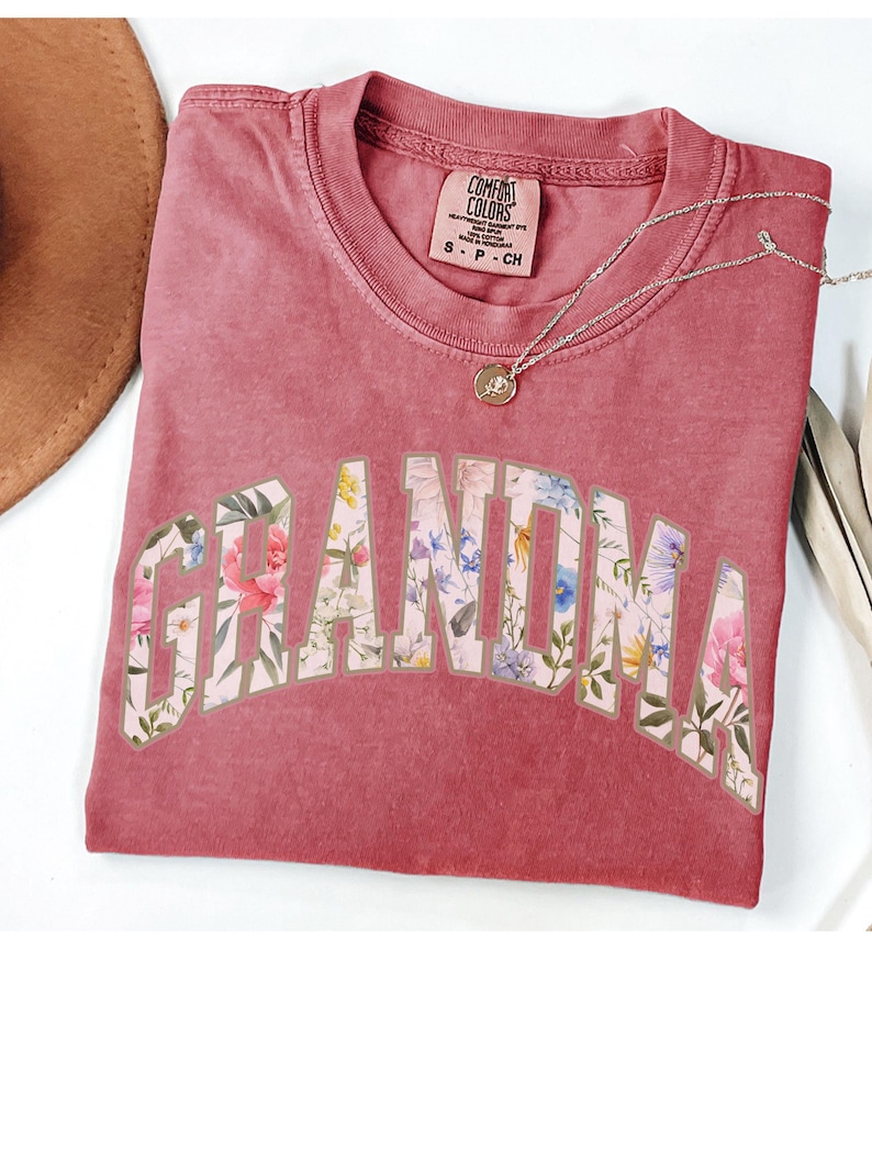 May include: A red t-shirt with the word "Grandma" printed in white with a floral pattern inside the letters. The shirt is made of a soft, comfortable fabric.