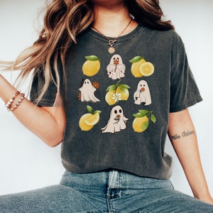 May include: A dark gray t-shirt with a graphic print of ghosts and lemons. The ghosts are white and have a flower in their hand. The lemons are yellow with green leaves.