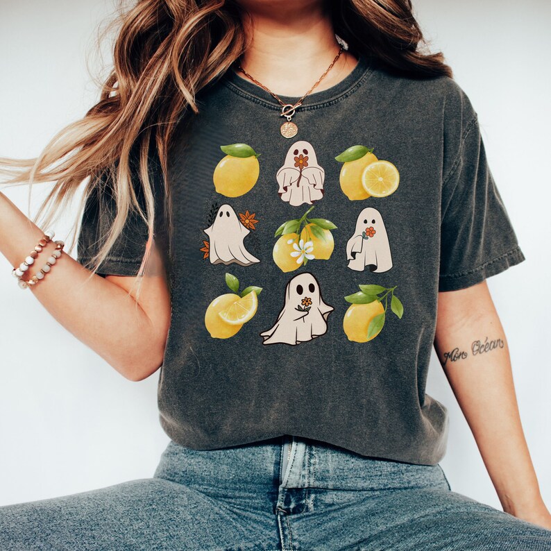 May include: A dark gray t-shirt with a graphic print of ghosts and lemons. The ghosts are white and have a flower in their hand. The lemons are yellow with green leaves.