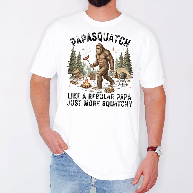 May include: White t-shirt featuring a Bigfoot illustration holding a sausage, with the text "PAPASQUATCH LIKE A REGULAR PAPA JUST MORE SQUATCHY". The design includes a campfire, trees, and a tent.