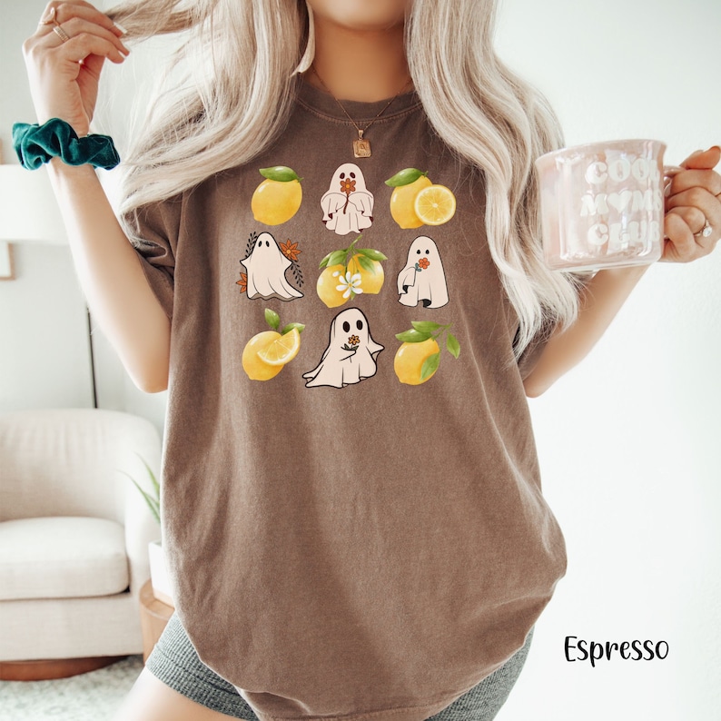 May include: A brown t-shirt with a graphic of white ghosts holding flowers and yellow lemons. The ghosts are surrounded by leaves and flowers.