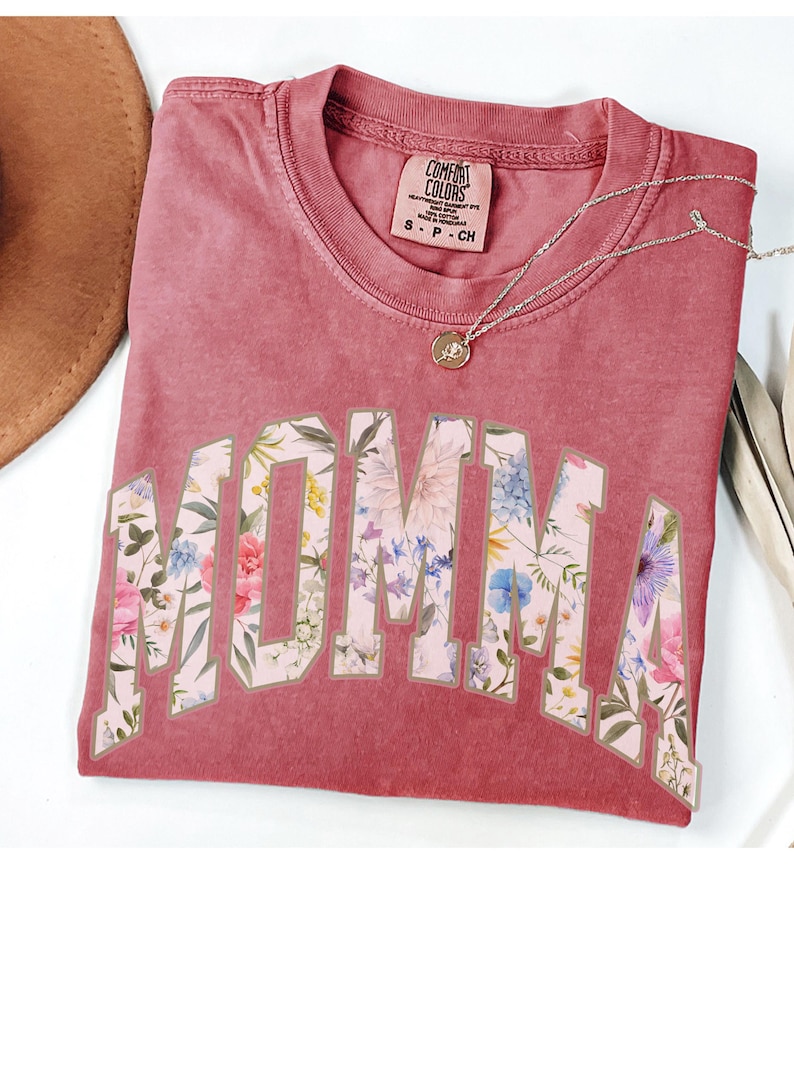 May include: A red t-shirt with a floral print design that says "MOMMA" in a large, white, outlined font.