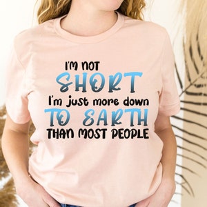 May include: A pink t-shirt with the text "I'm not short, I'm just more down to earth than most people" in black text with a blue gradient.