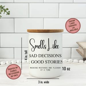 May include: A white candle with a bamboo lid, measuring 4 inches tall and 3 inches wide. The candle has the text "Smells Like Bad Decisions: Good Stories" printed on it. The candle is 10 oz and has the text "Masking mistakes one flicker at a time".