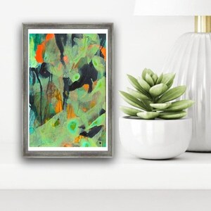 May include: Abstract painting in a gray frame with green, orange, and black colors. The painting is on a white shelf with a succulent plant in a white pot.