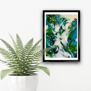 May include: Abstract art print in a black frame. The artwork features a blend of green, blue, and white watercolor-style paint. Splatter effects and layered brushstrokes create a dynamic composition. The print is displayed on a white wall next to a potted fern.