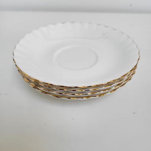 Puede incluir: Cuatro platillos blancos con un borde dorado apilados uno encima del otro.