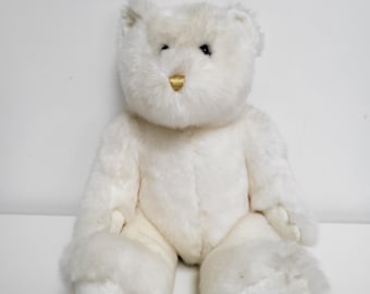 Può includere: Un orsacchiotto di peluche bianco con il naso dorato seduto su una superficie bianca.
