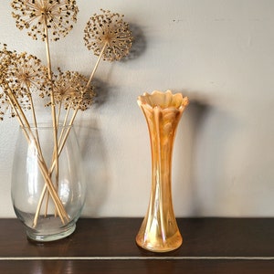 May include: A tall, iridescent orange glass vase with a flared top and a wavy design. The vase is sitting on a wooden surface.