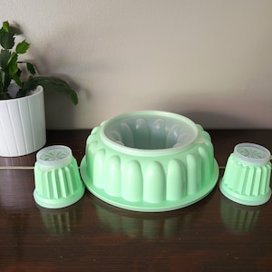 May include: A set of three green plastic moulds for making jelly desserts. The moulds are in the shape of a ring, and two smaller cups.