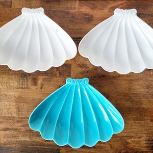 May include: Three ceramic seashell-shaped dishes. Two are white and one is turquoise blue.