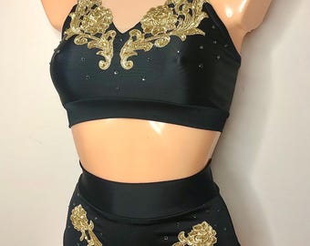 May include: A black two-piece dance outfit featuring a high-neck crop top with a nude mesh yoke and gold floral embroidery. The matching high-waisted bottoms are adorned with gold floral appliqués and scattered small crystals on both pieces.