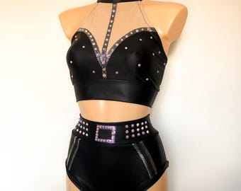 May include: A black two-piece dance costume with a halter top and high-waisted shorts. The top has a sheer mesh panel and is embellished with rhinestones. The shorts have a silver buckle detail and are also embellished with rhinestones.
