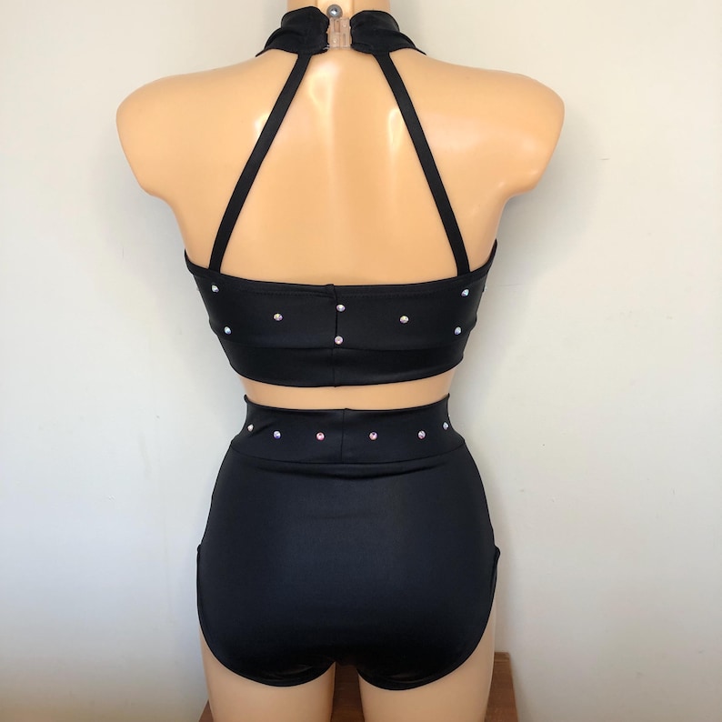 Puede incluir: Traje de baile negro con un top halter y pantalones cortos de cintura alta. El top y los pantalones cortos est&aacute;n adornados con pedrer&iacute;a.