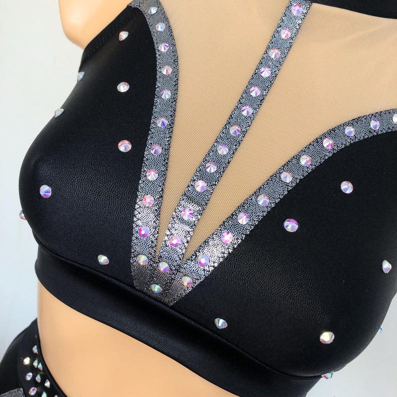 Puede incluir: Top de traje de baile negro con un panel de malla y ribete plateado. La parte superior est&aacute; decorada con diamantes de imitaci&oacute;n iridiscentes.