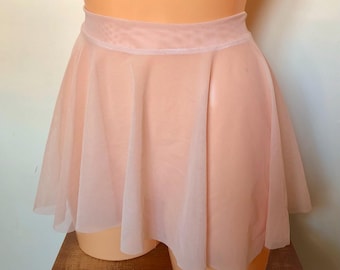 Puede incluir: Una falda de ballet de color melocotón claro con un diseño fluido. La falda tiene una cintura ancha y una silueta acampanada, hecha de una tela ligera y transparente. La falda está diseñada para la danza y las actuaciones.