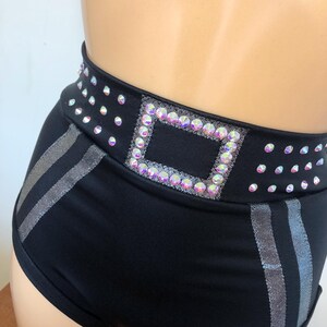 Puede incluir: Pantalones cortos negros de cintura alta con un detalle de rayas plateadas y un cintur&oacute;n de pedrer&iacute;a con una hebilla cuadrada.