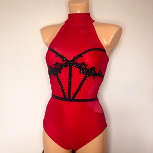 May include: Red leotard with a black lace and rhinestone bodice. The leotard has a high neckline and a halter strap design.