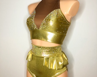 Puede incluir: Un traje de baile metálico dorado con un top halter y pantalones cortos de cintura alta. El top tiene un panel de malla transparente y ambas piezas están adornadas con diamantes de imitación.
