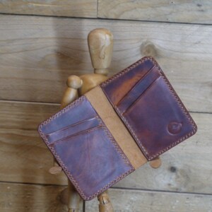May include: Open brown leather wallet with card slots and a bill compartment. The wallet has a distressed finish and contrasting stitching around the edges. The leather is a rich, warm brown colour.